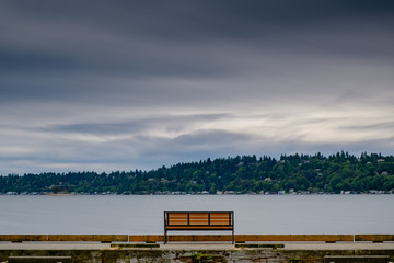 A lone bench looks out at a lake during an overcast day