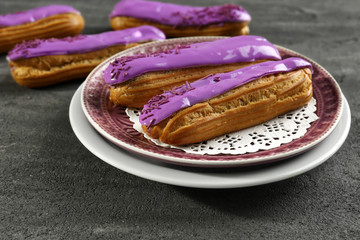 Plate with delicious glazed eclairs on dark textured background