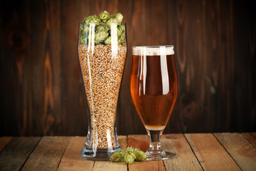 Glasses with beer, hops and malts on wooden background