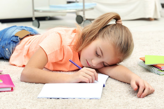 Attractive tired little girl lying on the floor with copybook