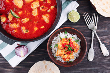 Chicken tikka masala in pan and portion with rice on wooden table