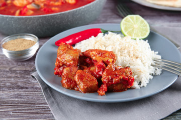 Portion of chicken tikka masala with rice in plate on grey wooden table
