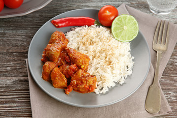Portion of chicken tikka masala with rice on grey wooden table