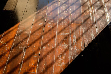sunlight from window with bars falling on wooden floor, wooden wall background in a morning light with shadows from a window frame