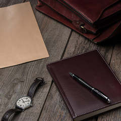 business accessories notebook, pen, rich portfolio, envelope, watch on wooden background