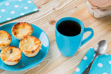 cheesecakes on blue plate, black tea in blue cup,  napkin at white polka dots, old spoon, sugar-bowl on wooden table