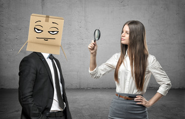 Woman is looking through a magnifier at a businessman with a box on his head with a pokerface