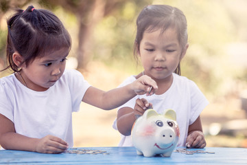 Child asian little girl putting coin into Piggy Bank in vintage color tone