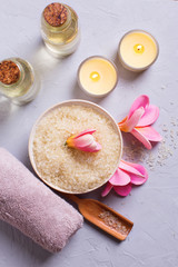 Sea salt in bowl, candles, towel and flowers on grey textured background.