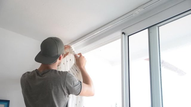 Young handsome man or handyman installing curtains over window at home, doing renovation work