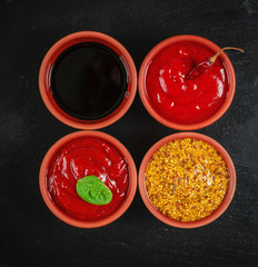 Four bowls of different sauces on black stone background. Grill sauce, tomato sauce hot Hungarian,...