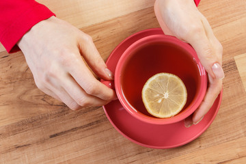 Hand of woman holding cup of hot tea on table