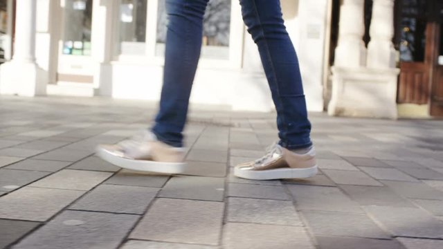 4K Camera follows the feet of a female walking through town, in slow motion