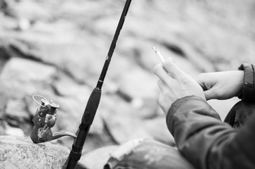 Fisherman hand with a cigarette close-up, waiting for a man smoking a cigarette looking at the bait