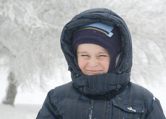 Funny smiling 5.5 y.o. boy on a winter park with trees covered by snow background - 137302277