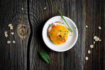 Fried Egg with Chives, Oat Flakes and Basil Leaf on Dark Wood Background.