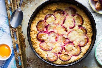 Plum Cake with Raw Cooking Ingredients on Wooden Kitchen Table. Overhead Shot.