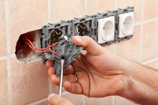 Electrician hands tighten electrical wires in wall fixture or socket