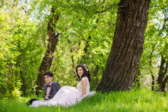 groom and bride sitting on the green grass
