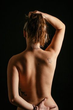 Chica mostrando  la espalda con tatuajes y con los brazos levantados. Foto de estudio con fondo negro.
