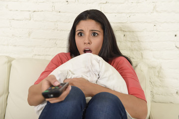 Naklejka premium latin woman sitting at home sofa couch in living room watching television scary horror movie