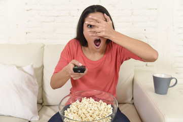 Naklejka premium latin woman sitting at home sofa couch in living room watching television scary horror movie