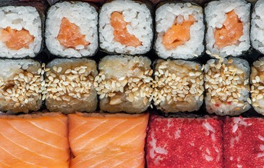 multicolored rolls and sushi rice, caviar and salmon, are on the table in the background