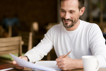 Delighted bearded man making notes in the cafe