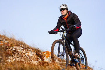 Cyclist in Black Jacket Riding the Bike on the Rocky Trail. Extreme Sport Concept. Space for Text.