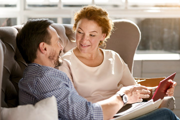 Smiling delighted middle aged couple relaxing at home