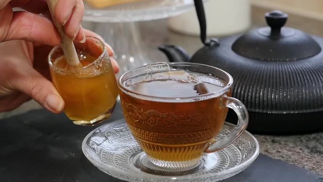 close up of woman adding honey to tea cup