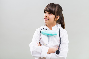 Beautiful little doctor thinking on grey background.