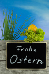 Osterdekoration, eine Holzwand mit einer Tafel Frohe Ostern, dahinter ein Osterei im Moos und ein...