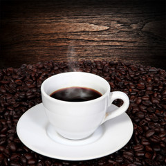 Black coffee and coffee beans with smoke on wood