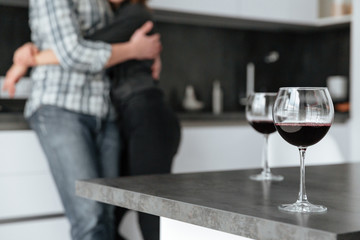 Loving couple standing in kitchen. Focus on alcohol in glass.