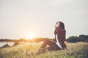 Young hipster woman sitting on grass near the lake relaxing enjoy with fresh air.