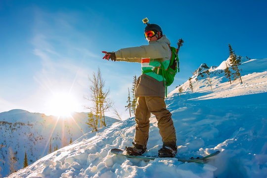 Freeride snowboarder stands on hillside at dawn and shows his hand forward