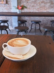 In the cafe, Coffee with Latte Art in white cup and biscuit on wooden table.
