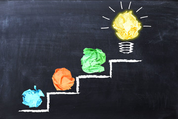 Evolving idea concept with colorful crumpled paper and light bulb on steps drawn on blackboard