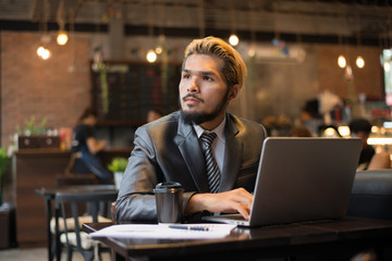 Young businessman holding cup of coffee while working on laptop computer in coffee shop.