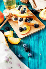 
sweet snack , bruschetta with berries and fruits , blueberries , blackberries and peaches , with butter and honey on wooden background