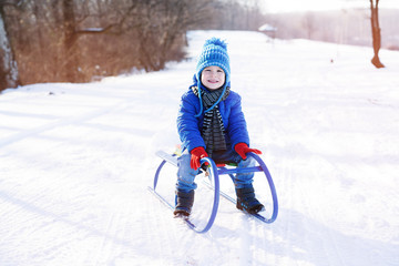 Fototapeta na wymiar Little boy enjoying a sleigh ride. Child sledding. Toddler kid riding a sled. Children play outdoors in snow. Kids sled in winter park. Outdoor active fun for family vacation.