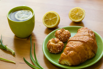 Tea with lemon and croissant for fresh spring breakfast on wooden table