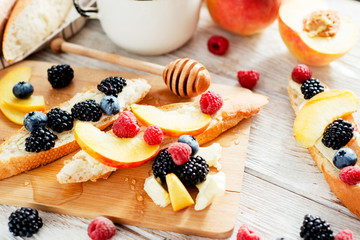 sweet snack , bruschetta with berries and fruits , blueberries , raspberries, blackberries and peaches , with butter and honey on wooden background