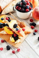 sweet snack , bruschetta with berries and fruits , blueberries , raspberries, blackberries and peaches , with butter and honey on wooden background