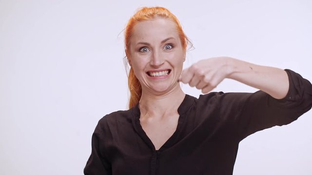 Middle-aged Caucasian female with colored orange hair and dark brown shirt sleepy cleaning teeth with imaginary dental brush on white background in slowmotion