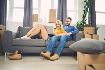 Obraz premium couple in new apartment using laptop. Lot of moving boxes around them
