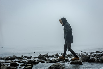 Man in the mist walking on the lake ice in winter afternoon. Peaceful atmosphere. Foggy air.