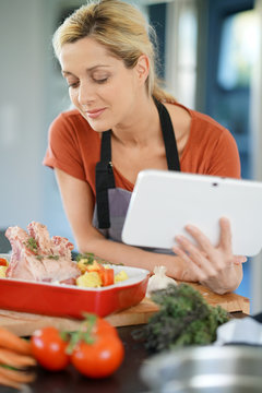 Woman in domestic kitchen reading cooking receipe on tablet