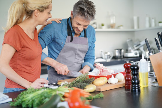 Middle-aged couple having fun cooking together in home kitchen